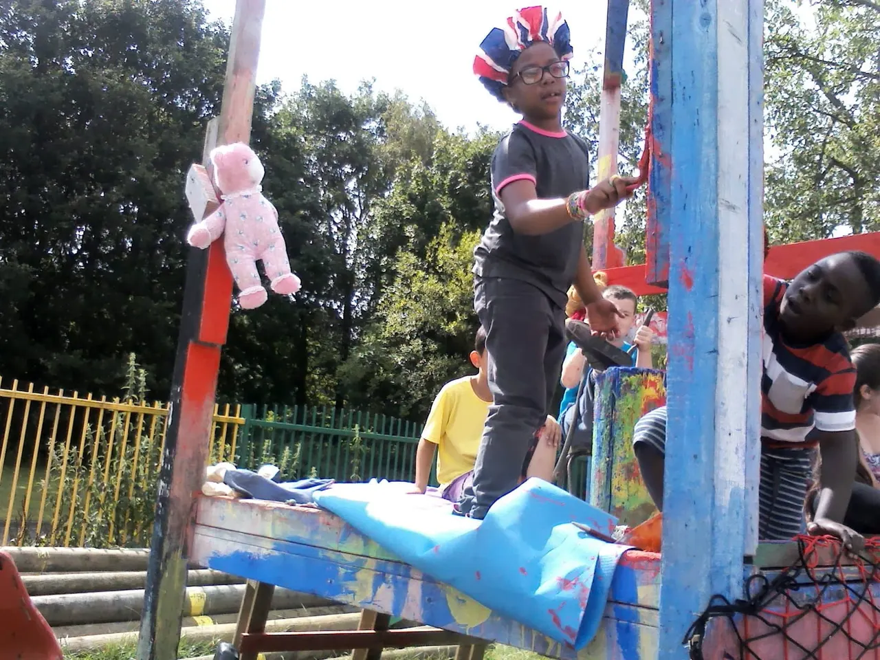 Child wearing cycling helmet and safety gear performing on colourful playground equipment whilst other children watch.