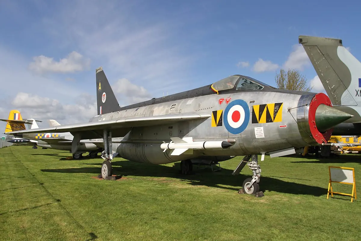 Vintage military jet aircraft with RAF roundels displayed on grass alongside other aircraft.
