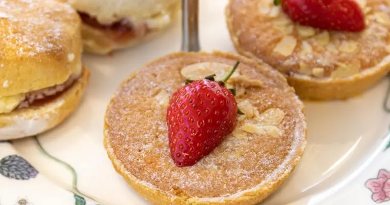 Assorted pastries topped with icing sugar, sliced almonds and fresh strawberries on a decorative plate.