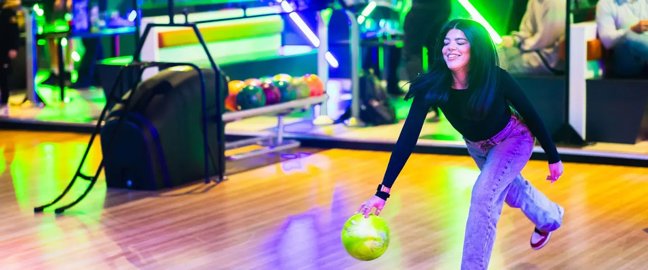 Young woman bowling with a glowing neon ball on a brightly lit lane in an indoor bowling alley.