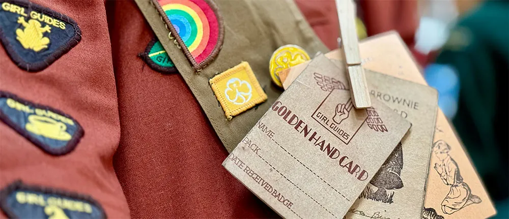 Close-up of Girl Guides uniforms with colourful badges and Golden Hand Cards attached to sashes.