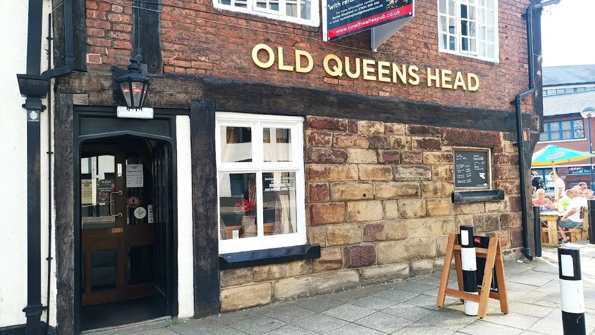 Traditional brick pub frontage with dark wooden door, white-framed windows, and golden signage on red brick exterior.