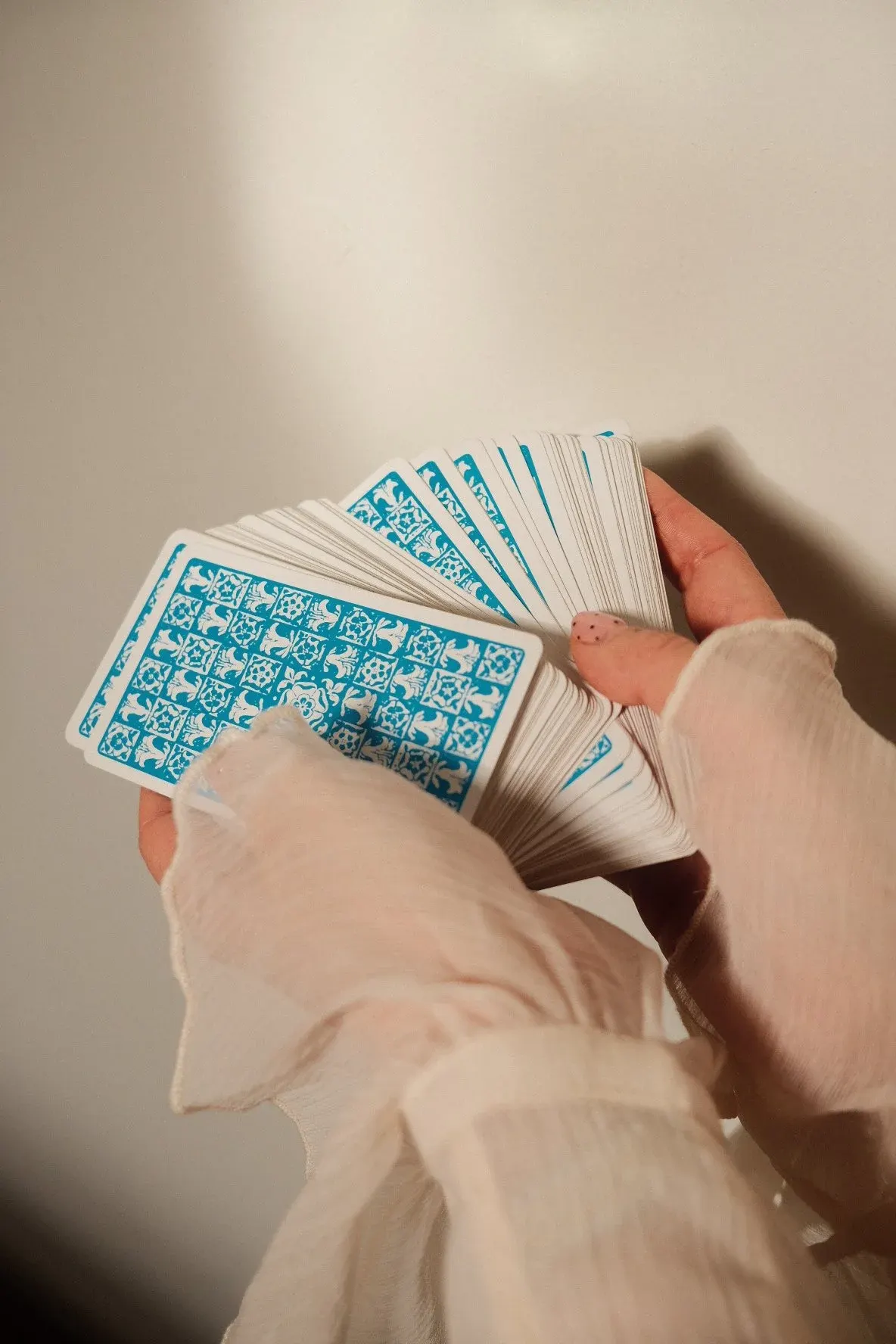 A person's hands holding and fanning out a deck of playing cards with turquoise patterned backs.