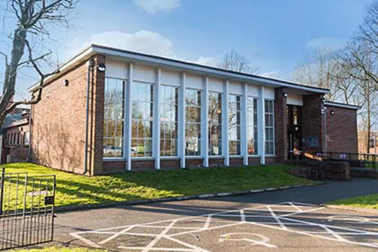 Modern brick library building with large windows and green lawn under blue sky with bare winter trees.