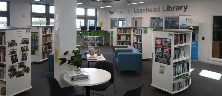 Modern library interior with bookshelves, reading tables, seating areas and natural light from large windows.