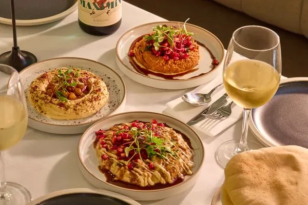 Table setting with three plates of drizzled savoury pancakes, white wine glasses, and cutlery at a restaurant.