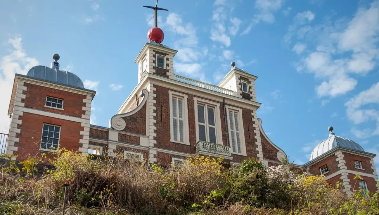 Historic red brick building with twin domed towers topped with a cross and red sphere, set against blue sky.