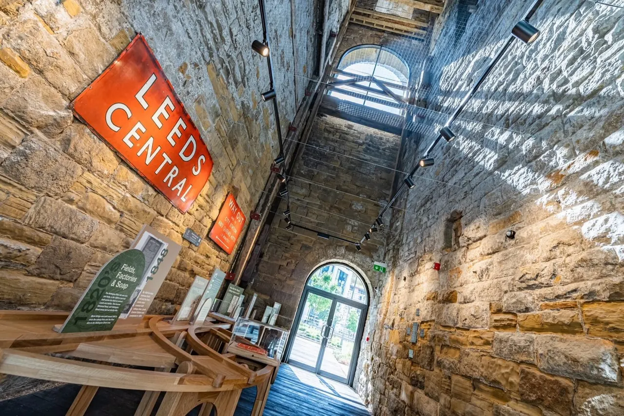 Interior of a stone-walled museum corridor with an orange "Feeds Central" sign and wooden display pieces.