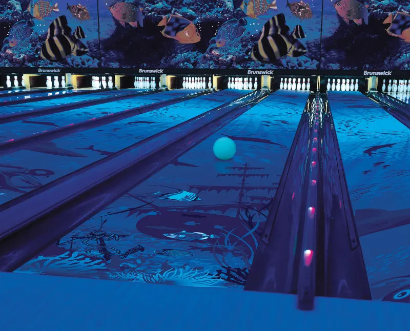 UV glow bowling lanes with underwater murals and a neon blue ball rolling toward the pins
