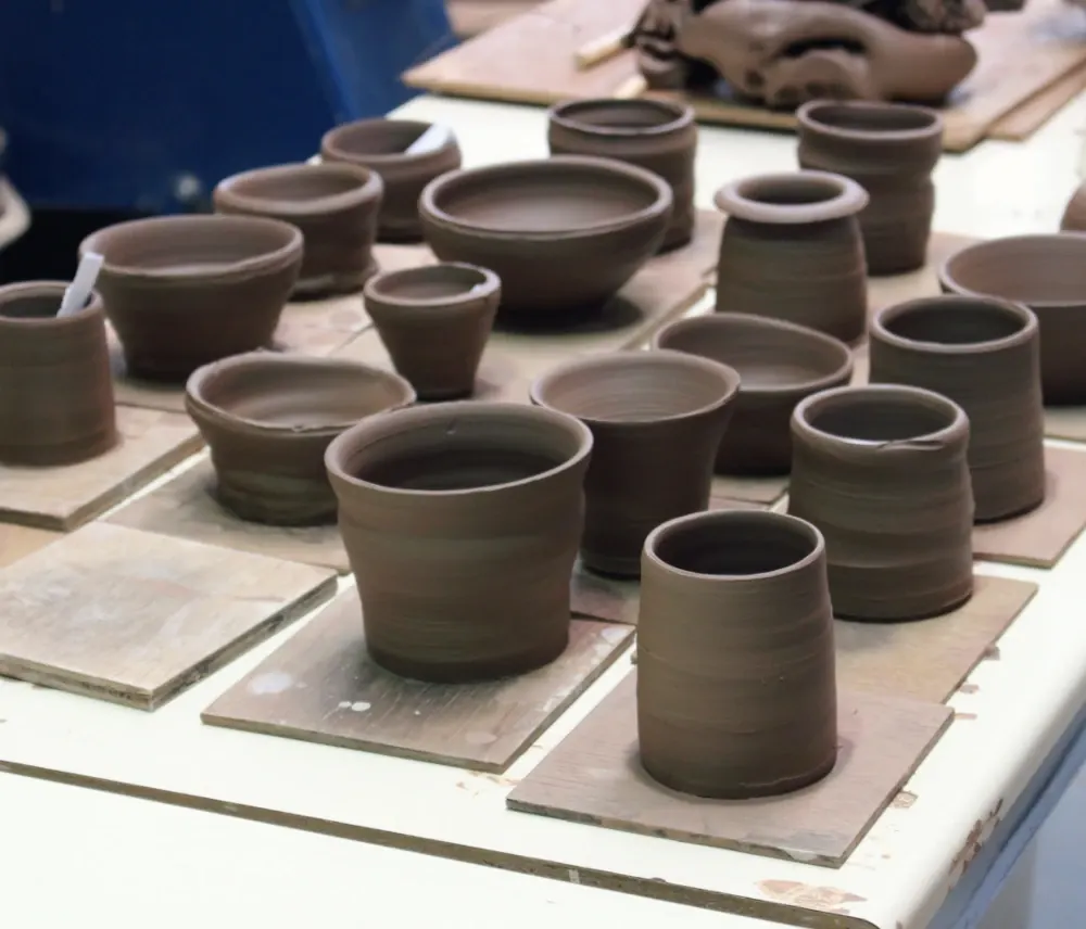Handmade ceramic vessels and bowls displayed on wooden boards at a pottery workshop.