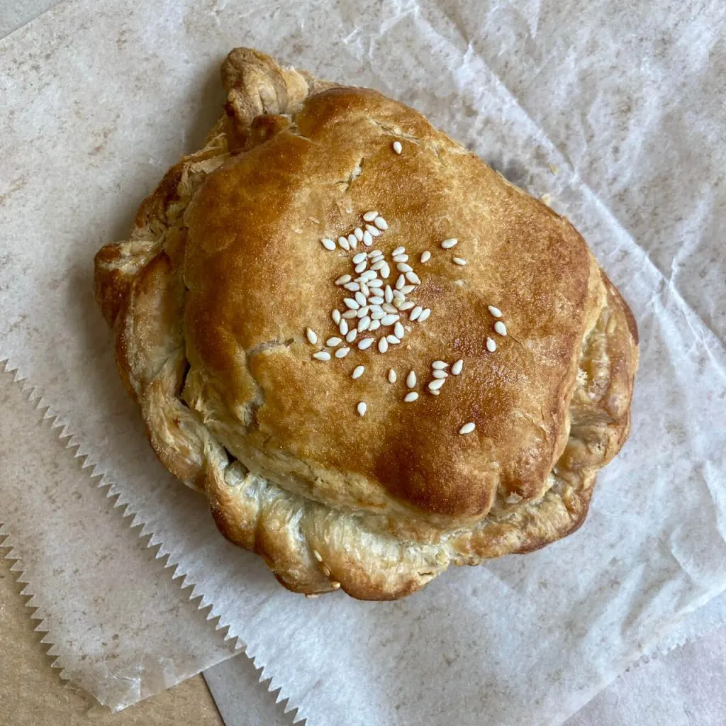 Golden-brown seeded bread roll on white paper.