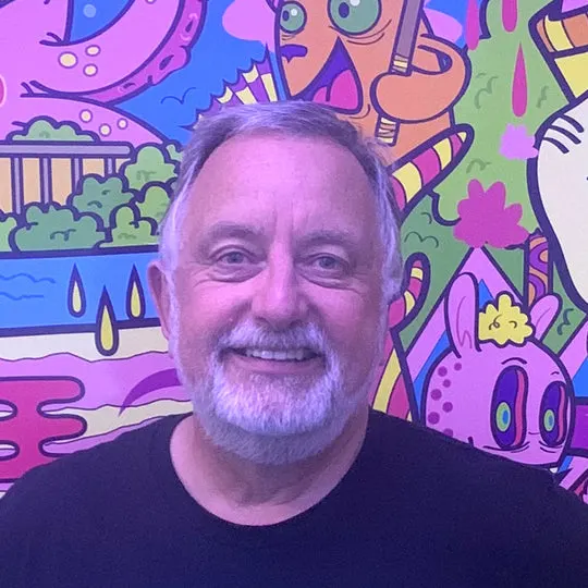 Man smiling at camera in front of colourful abstract mural artwork.