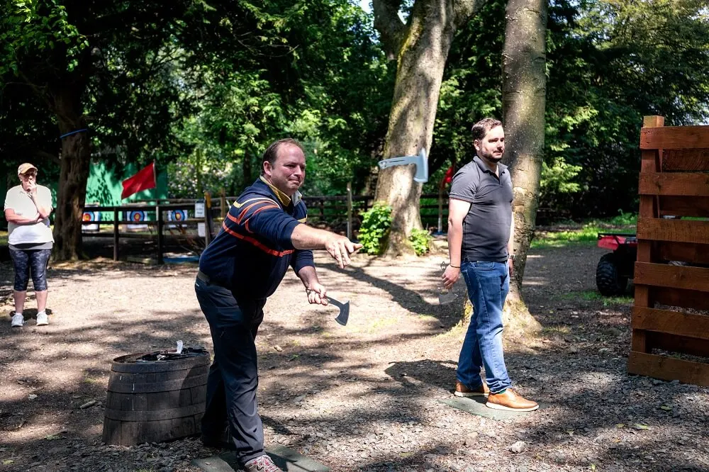 Adults playing axe throwing at an outdoor woodland activity centre.