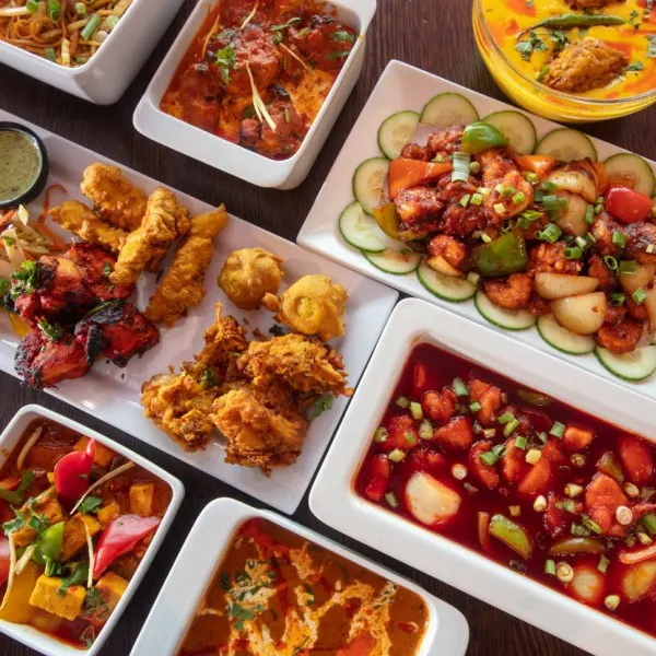 Overhead view of an Asian banquet spread with fried dishes, curries, and stir-fried vegetables on white plates.