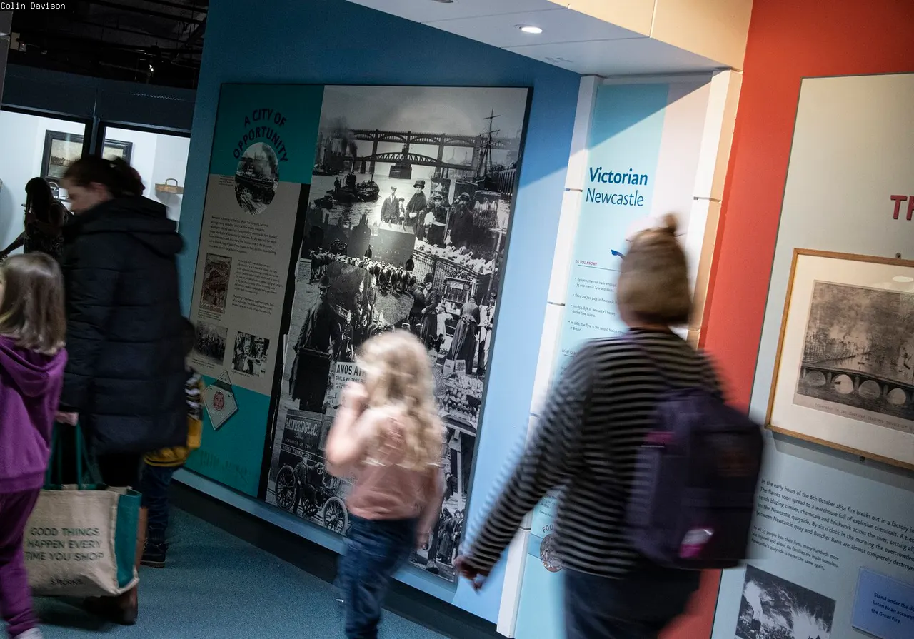 Visitors browsing historical exhibition displays about Victorian Newcastle in a museum gallery.
