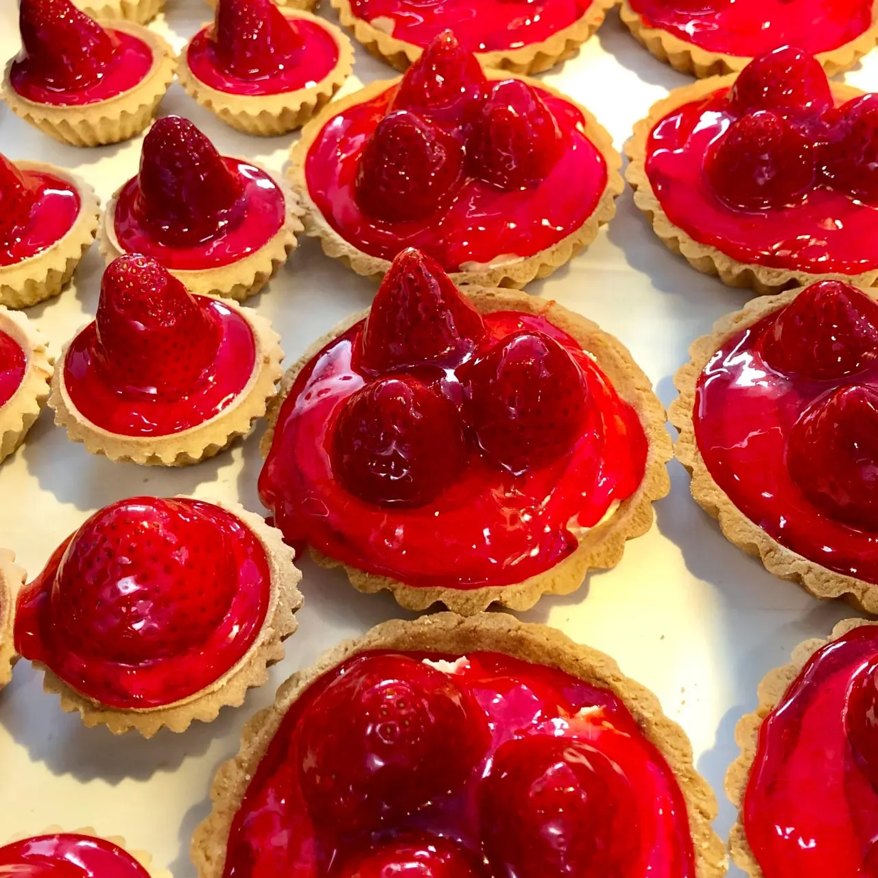 Individual pastry tarts with glazed red berries on cream filling and fluted pastry cases.
