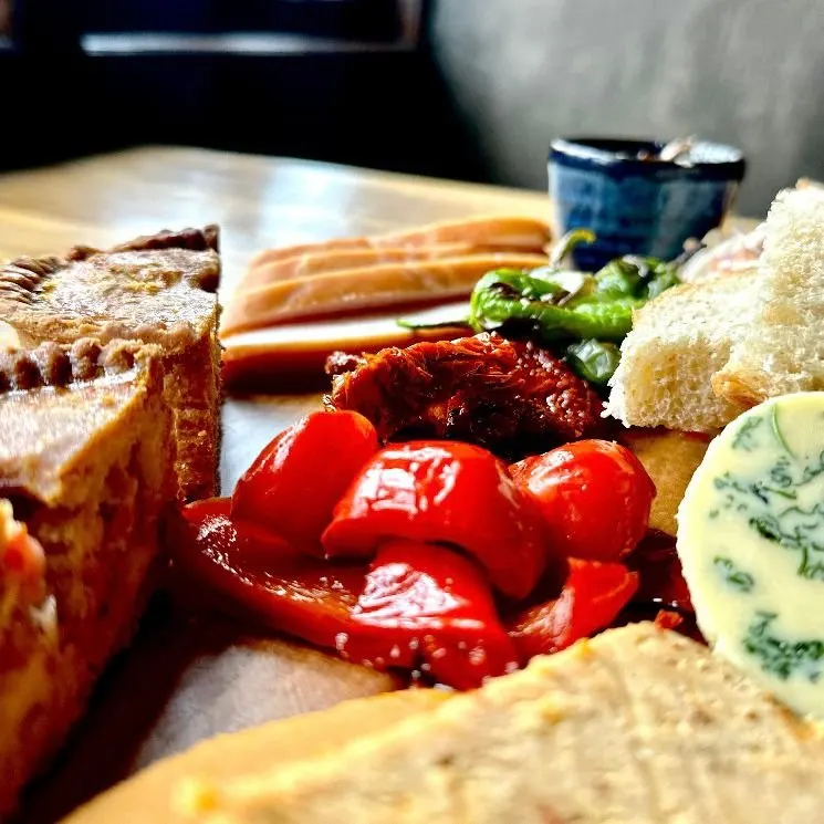 Charcuterie board with cured meats, bread, roasted peppers, and green chillies arranged on a plate.
