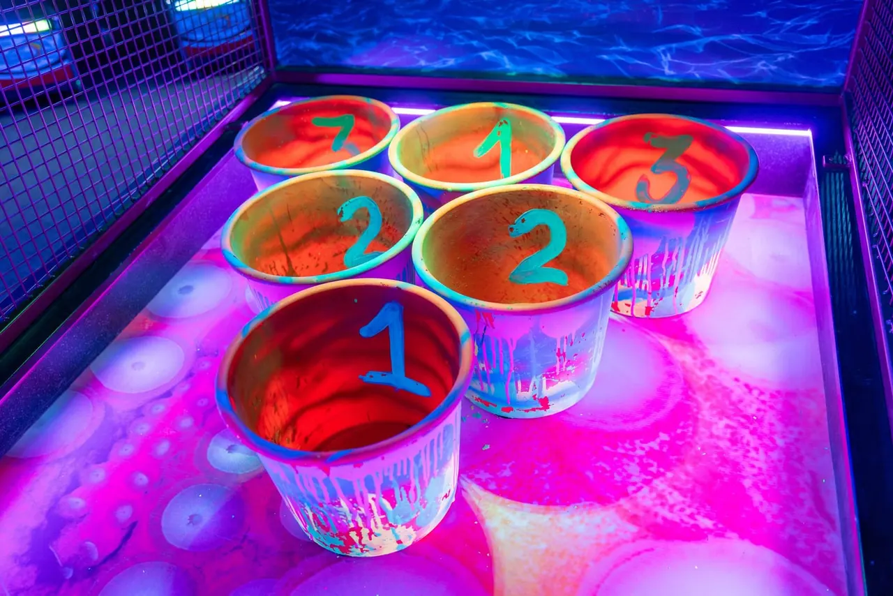 Colourful neon-lit game pods with numbered basins under bright purple and blue lighting in an indoor leisure activity arena.