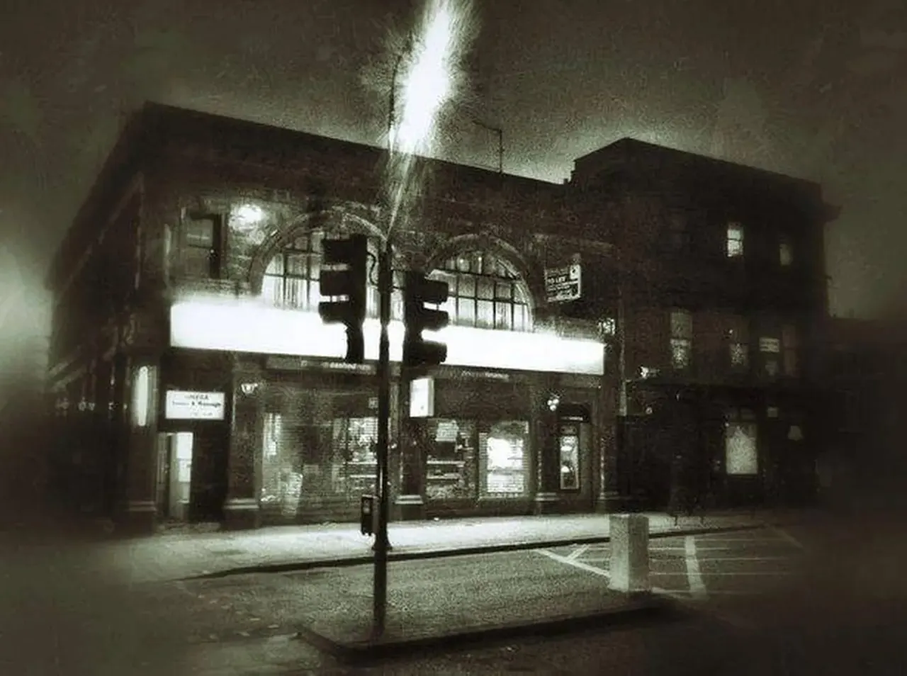 A brick building at night with illuminated shopfronts and a street lamp in the foreground.