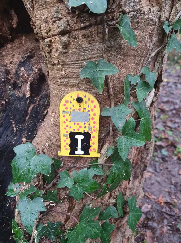 A bright yellow birdbox with red spots mounted on a tree trunk surrounded by ivy leaves.
