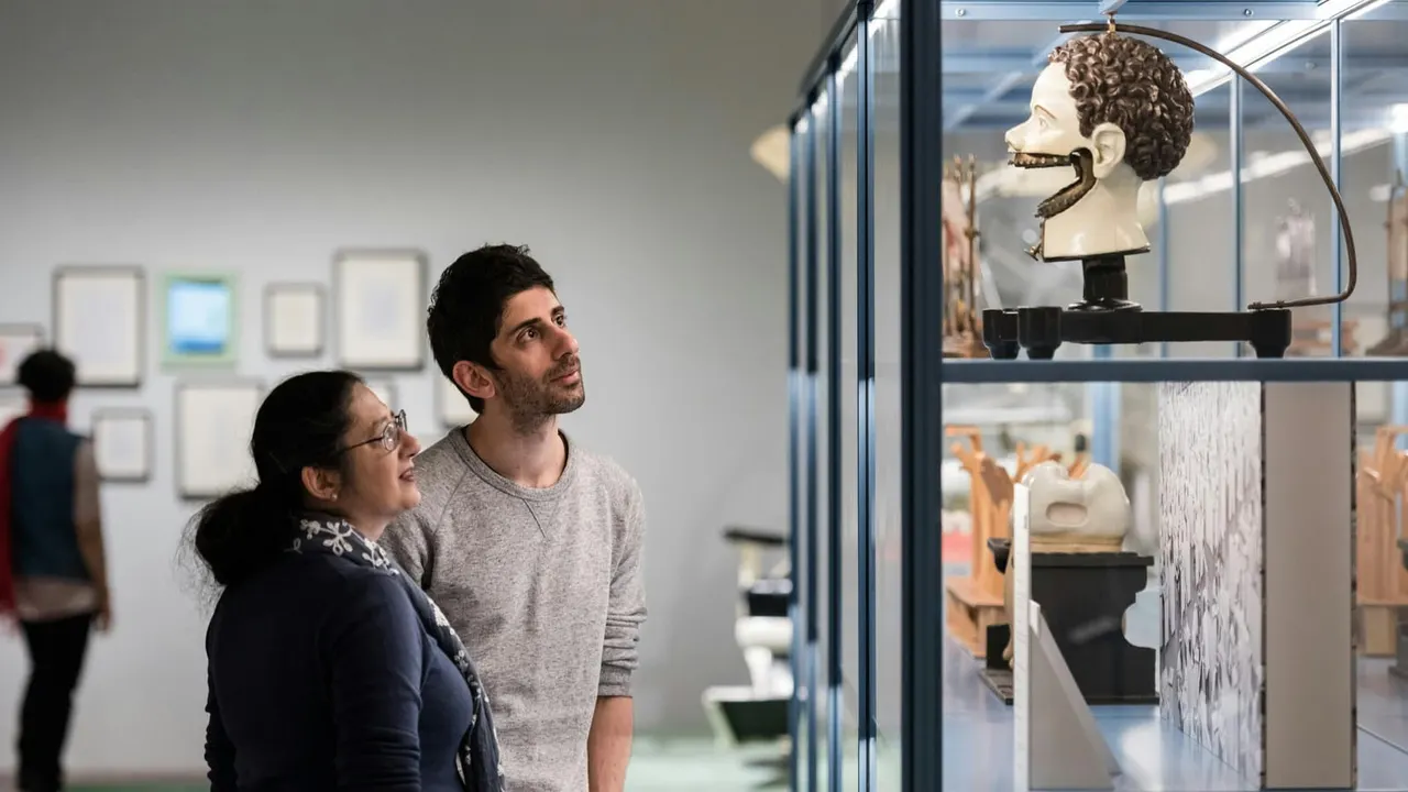 Two visitors viewing a classical bust sculpture displayed in a museum gallery case.
