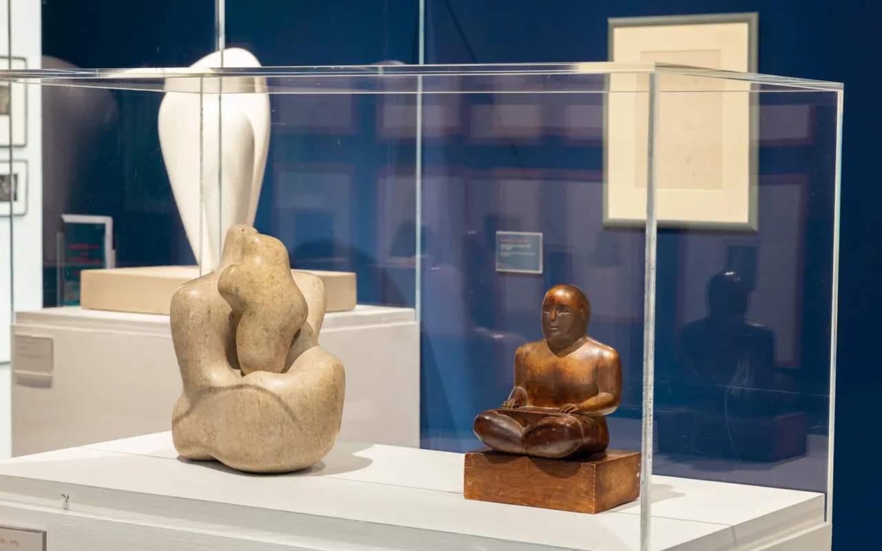 Stone and wooden sculptural figures displayed in a glass case within a gallery setting.