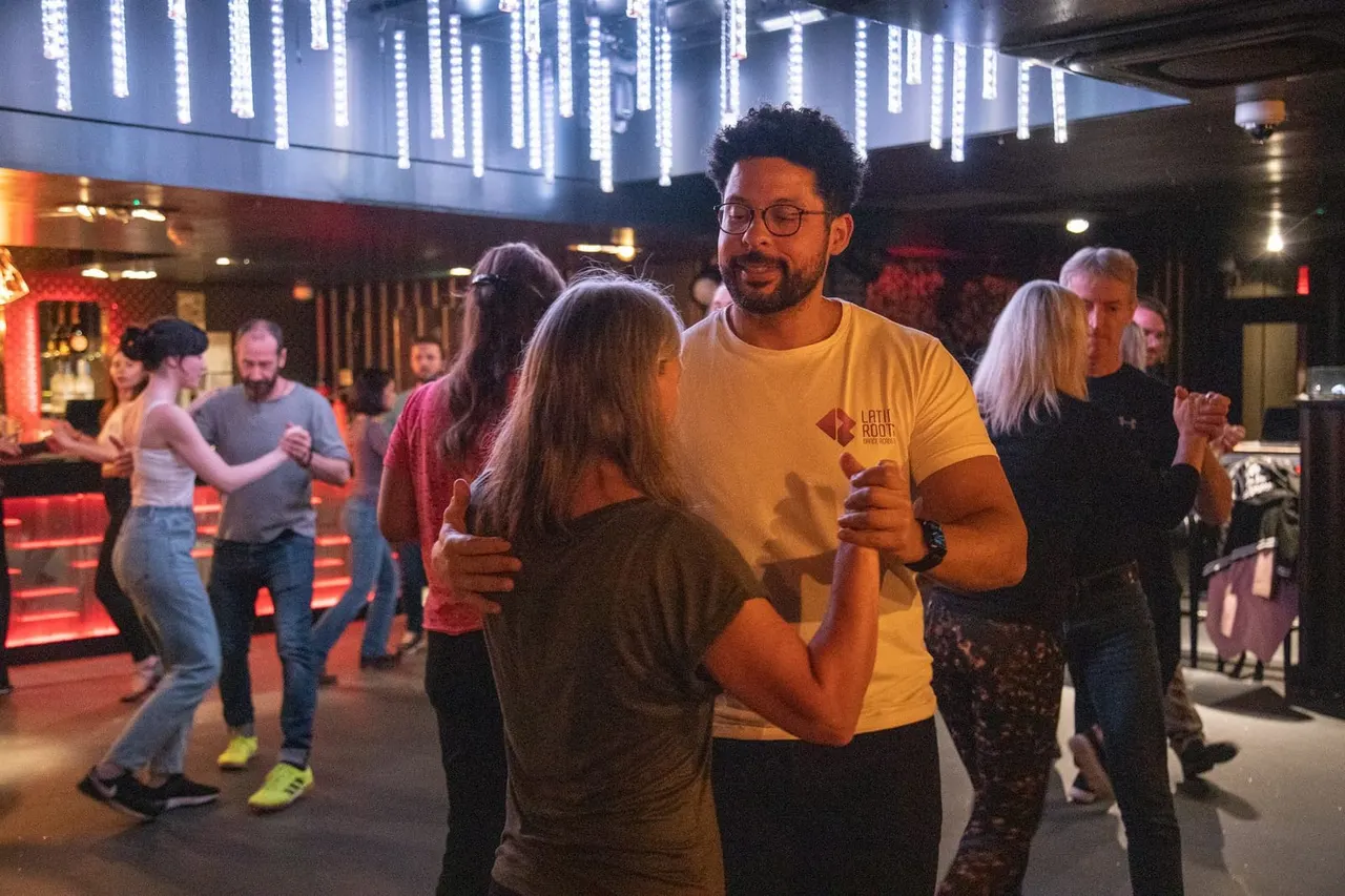 Groups of people dancing together in a modern indoor venue with red ambient lighting and overhead LED decorations.