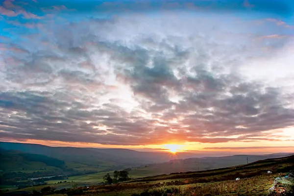 Sunset over rolling moorland and valley landscape with dramatic cloudy sky.