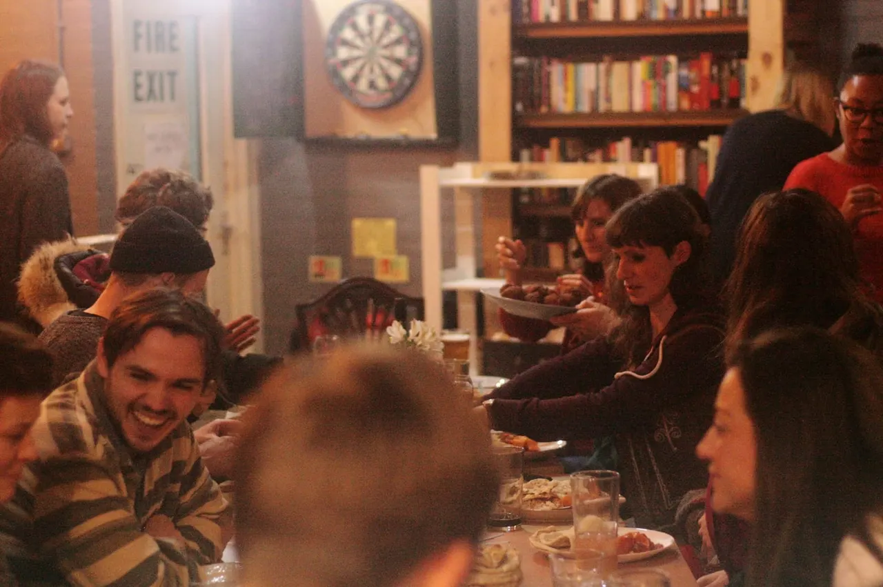 Group of people dining and socialising together in a warm, book-lined interior venue.