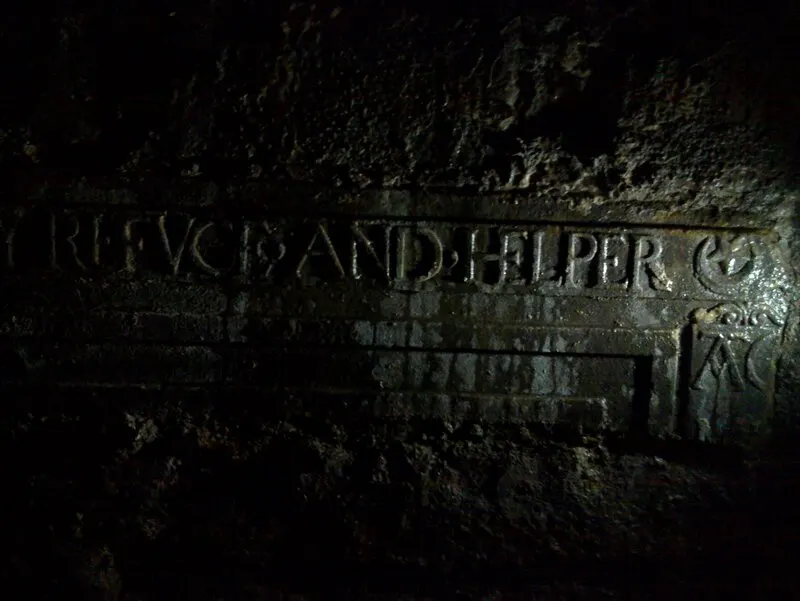 Ancient Roman inscription carved into stone wall in dimly lit underground chamber.