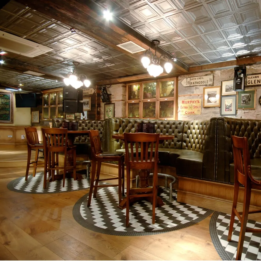 Interior of a traditional Irish pub with wooden bar seating, decorative tiles, vintage signage, and period lighting.