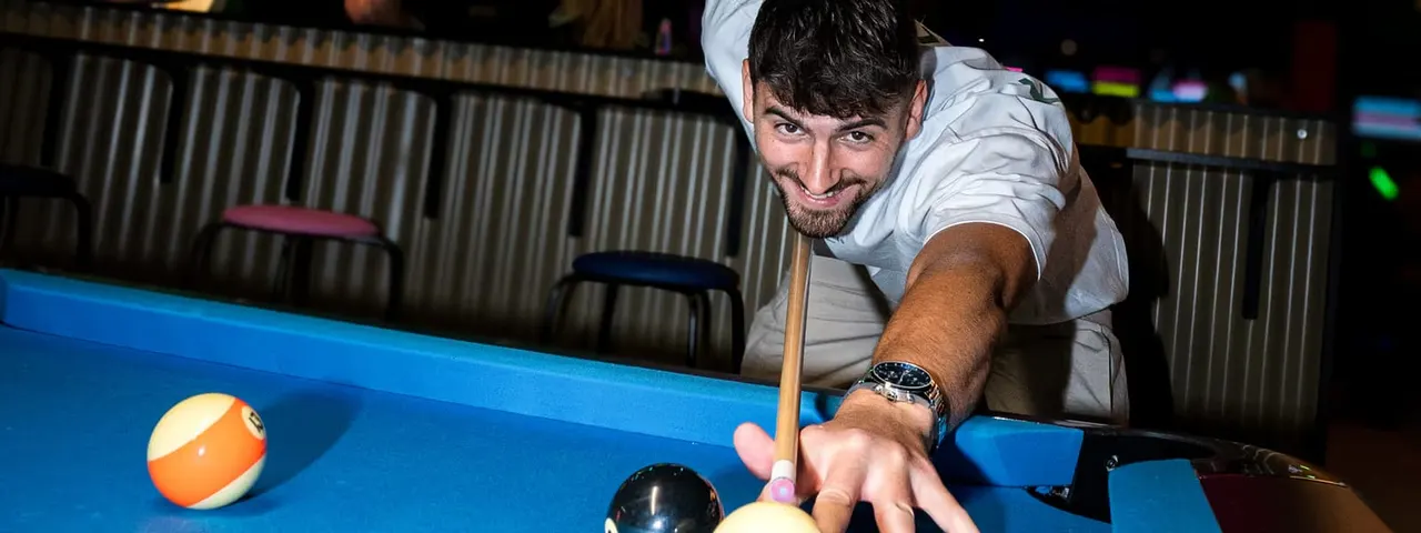 Man playing pool, leaning over blue table with cue and striped balls.