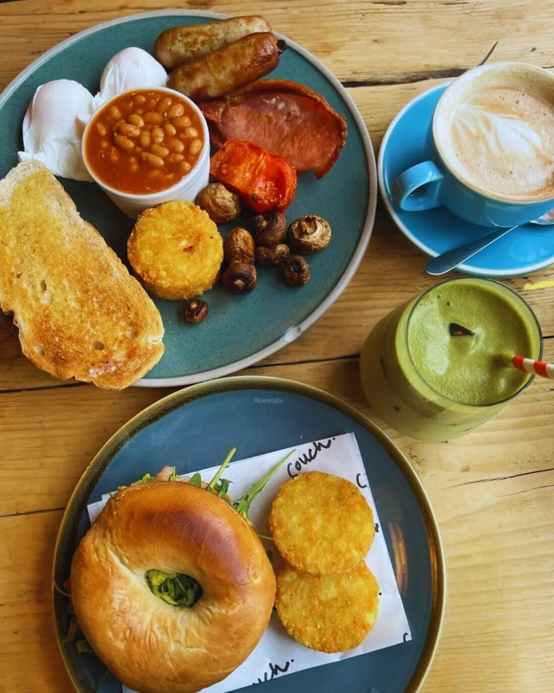 Full English breakfast with sausages, bacon, eggs, beans and toast, alongside a bagel with crisps, cappuccino and green smoothie.