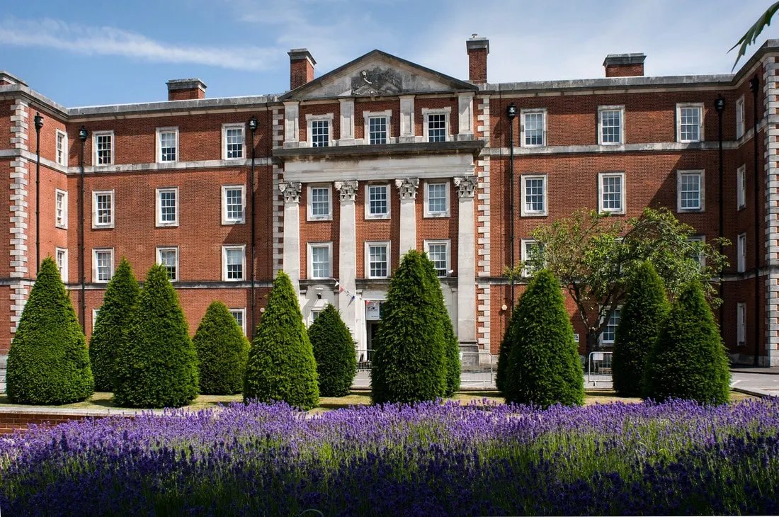 Red brick Georgian building with purple lavender flowers and topiary in the formal garden forecourt.