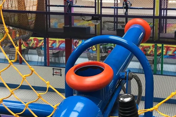 Colourful play equipment including a blue tube slide with orange rings in an indoor play centre.
