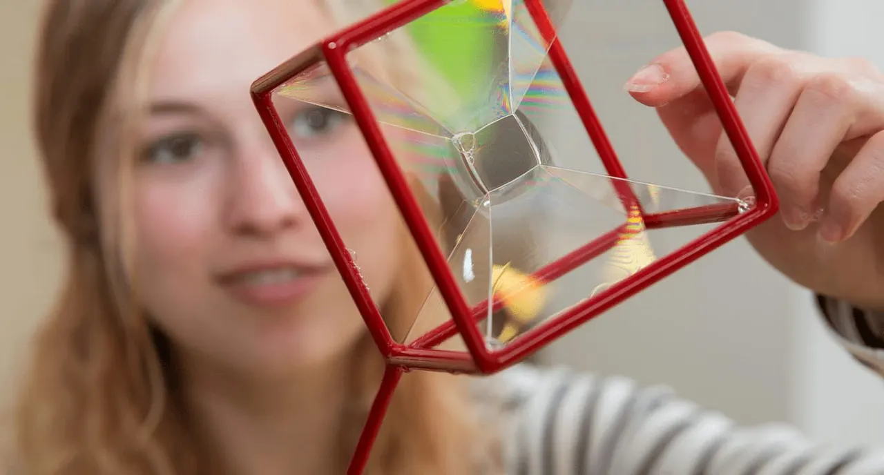 Woman holding a red geometric prism that refracts light into rainbow colours.