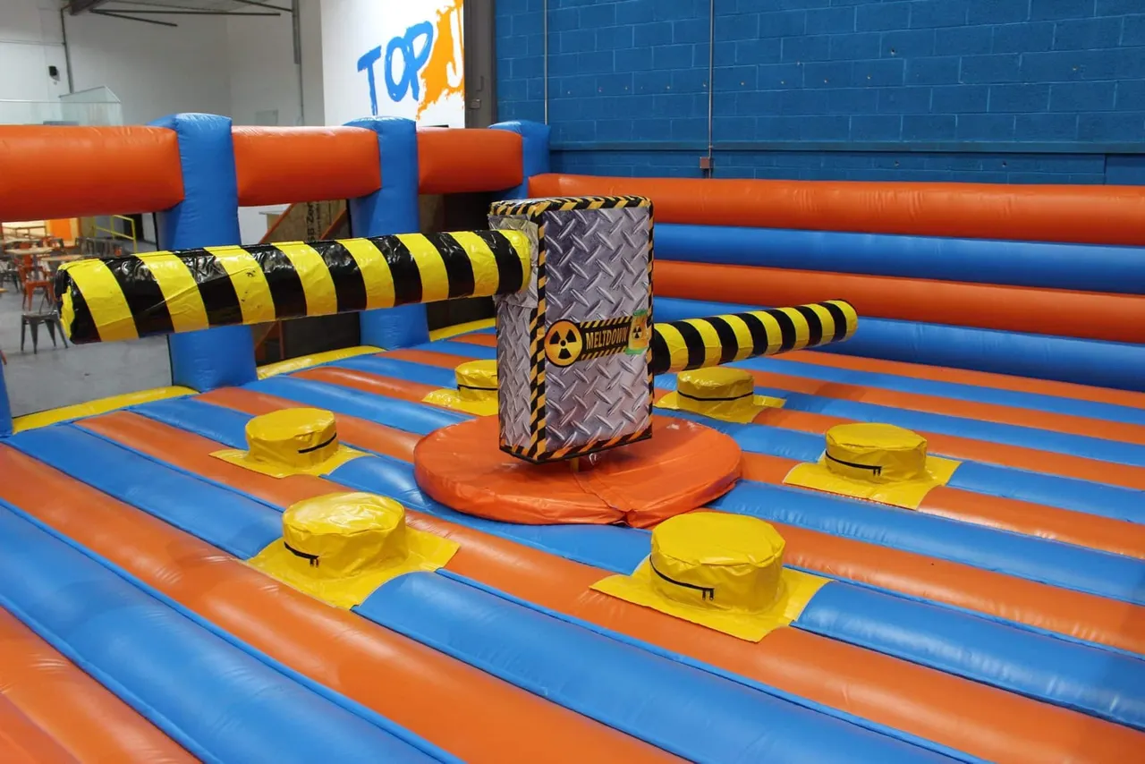 Inflatable obstacle course with yellow and black striped tunnels, yellow airbags and a central padded column in an indoor play arena.