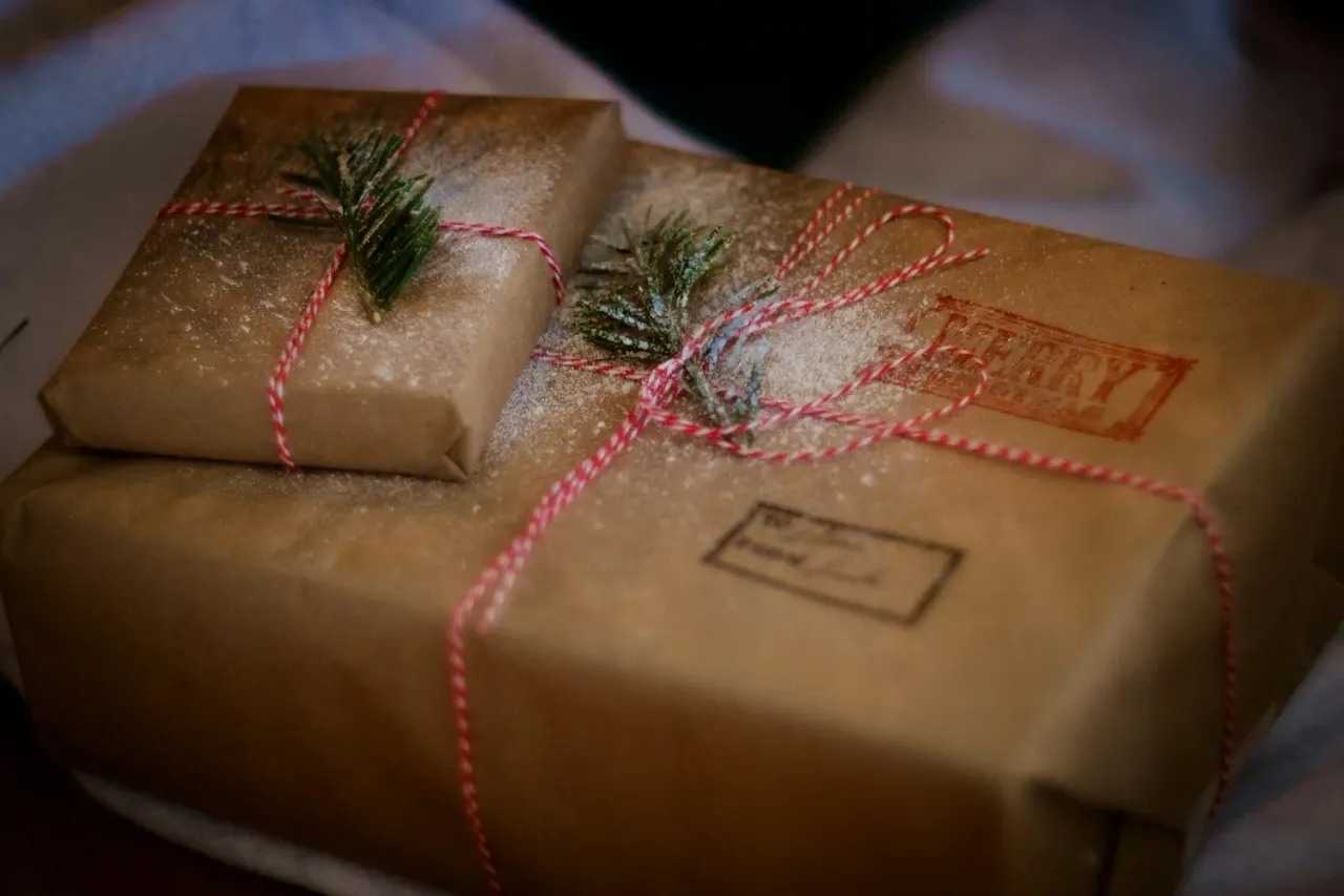 Two kraft paper parcels tied with red and white twine, decorated with sprigs of evergreen and dusted with snow.