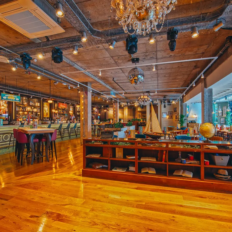 Spacious bar interior with wooden beams, chandeliers, nautical décor and shelving, lit by warm lighting.