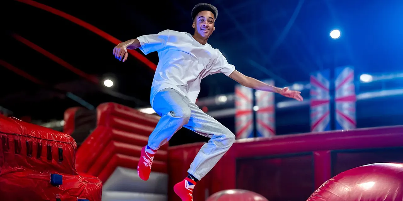 Young man leaping between red inflatable obstacles on an indoor activity course with blue lighting.