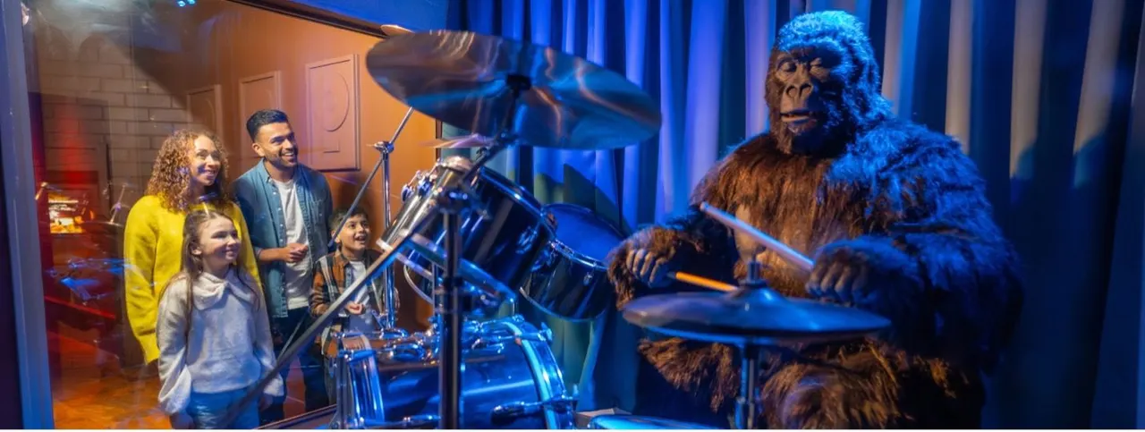 Family watching an animatronic primate figure play drums in a themed exhibition display.