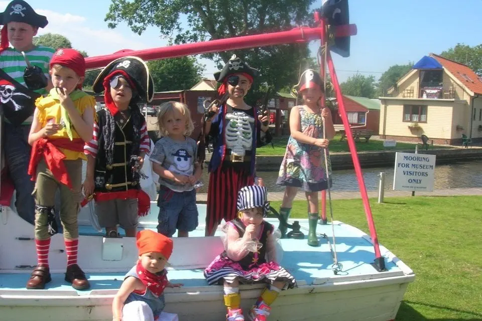 Children in pirate costumes standing on and around a boat moored at the waterside during a themed activity day.