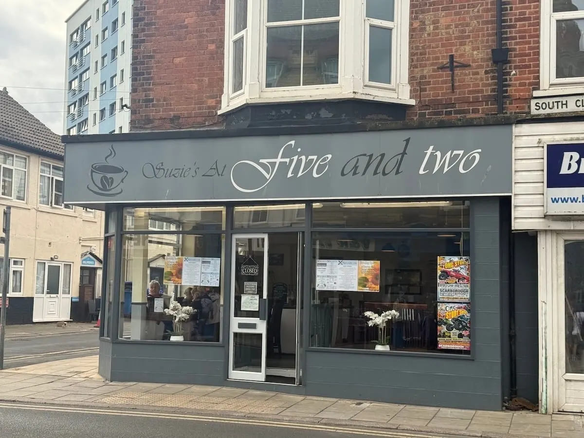 Storefront of Susie's At Five and Two café with grey fascia, large windows, and customers visible inside.