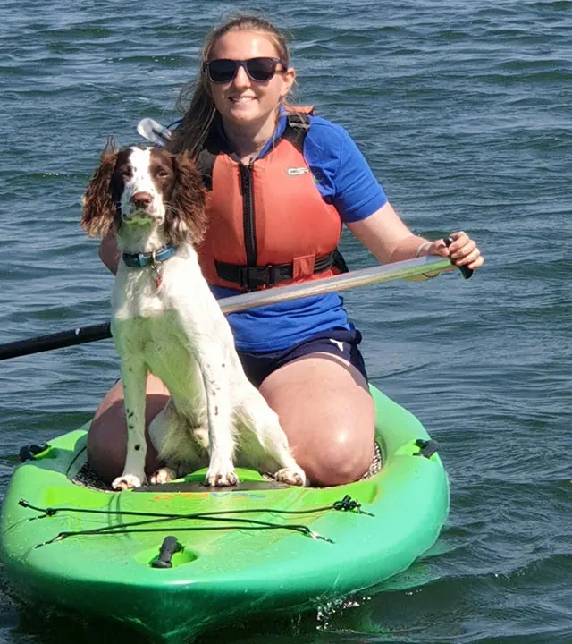 Woman and spaniel paddleboarding on a green inflatable board on calm sea water.