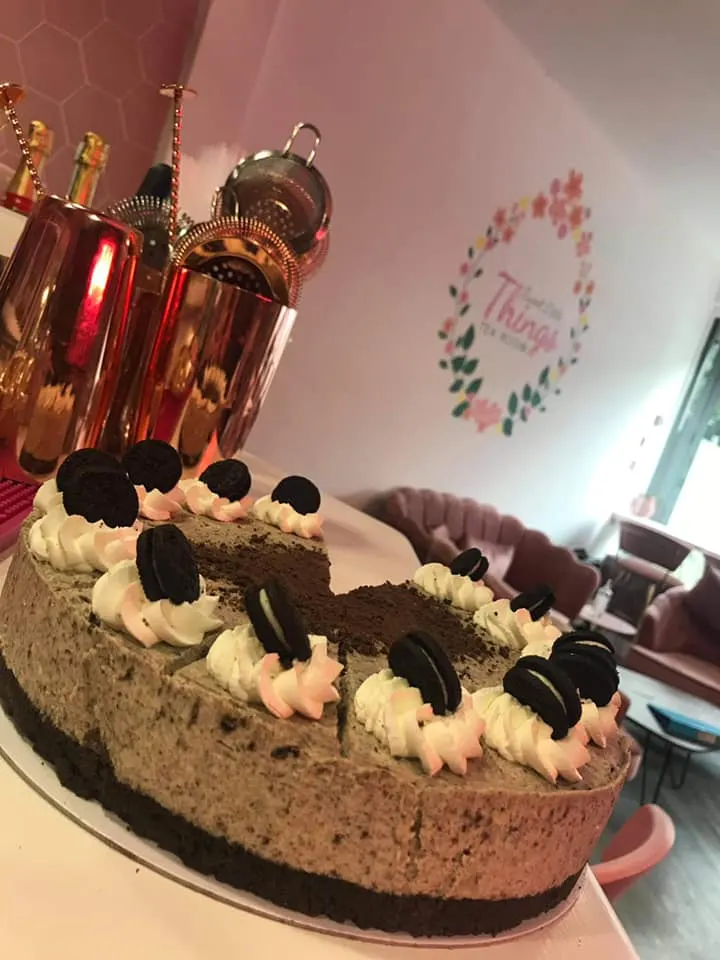 Chocolate cake decorated with cream and biscuits, displayed in a pink-themed tea room with perfume bottles.