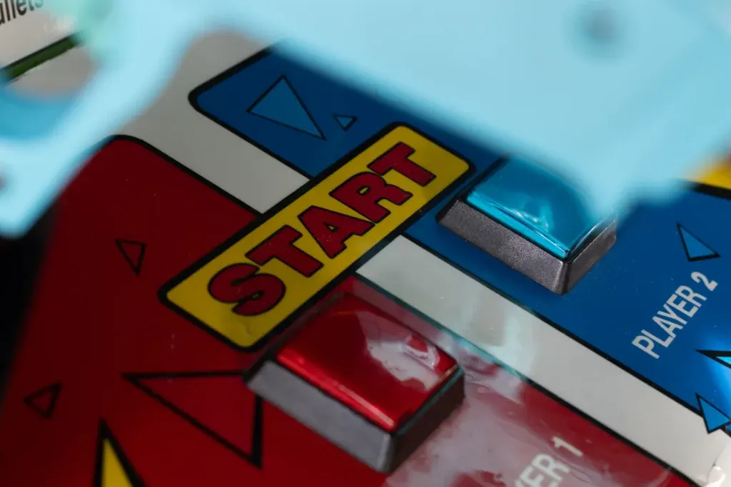Close-up of a arcade game control panel showing a "START" button in yellow with red text, alongside blue and red player buttons.