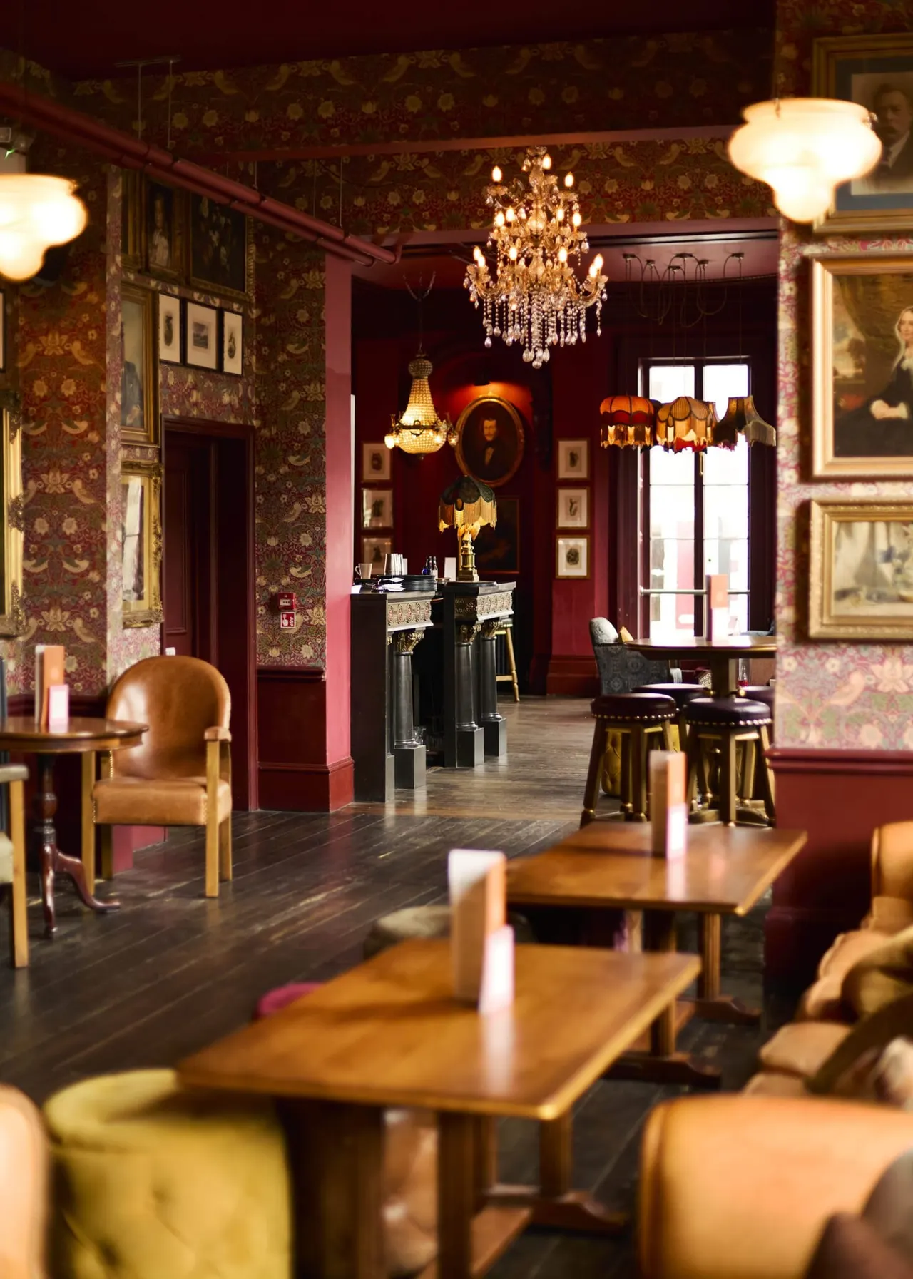 Ornate lounge interior with deep red walls, period wallpaper, chandeliers, wooden furniture and framed artwork.