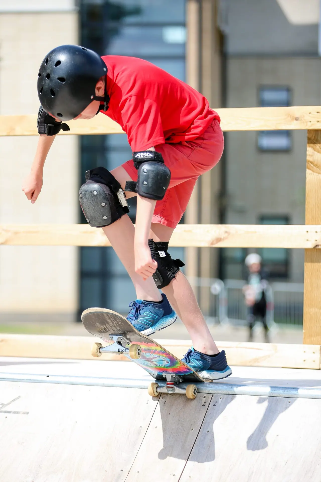 Young person performing a skateboard trick over a wooden ramp whilst wearing protective gear.
