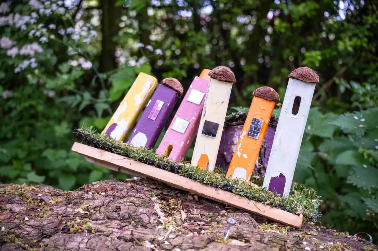 Colourful miniature painted houses with thatched roofs arranged on a mossy log in woodland.