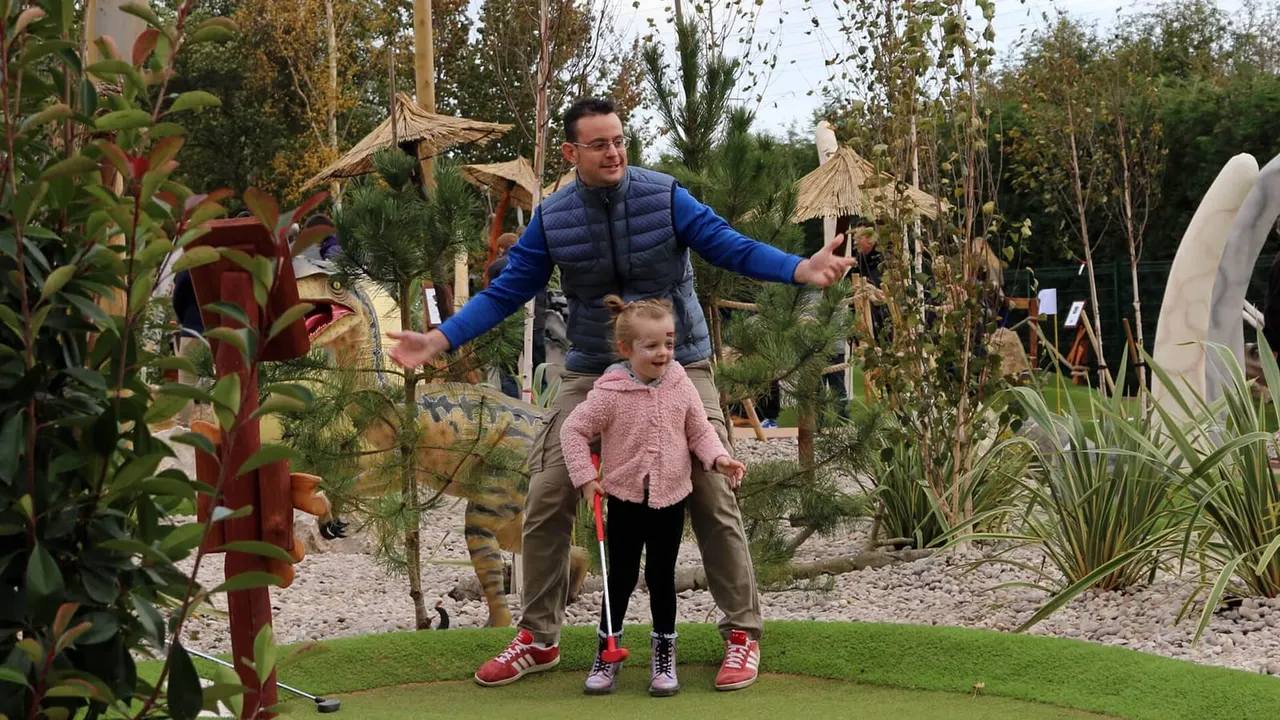 Dad and child putting beside raptor statue on Lost World outdoor course